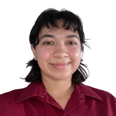 A picture of Diana, a young Hispanic woman, from the chest up. She is seen wearing an unbuttoned blouse and relaxed hairstyle that frames her face. A close-lipped smile is also presented.