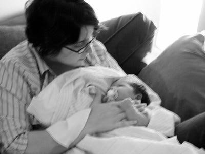 black and white, slightly blurry image of woman holding infant. woman in partial profile looking down. kid has pacifier in