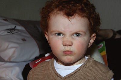 young boy with angry expression. red hair, white skin, brown sweater
