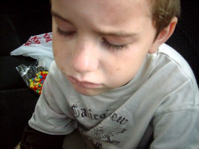 Photo of a boy with a sad expression taken from above. pale skin, freckles, brown hair, grey t-shirt.