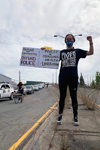 Wearing Black Lives Matter shirt & holding sign: Defend our communities, defund police. Invest in housing, health, liberation