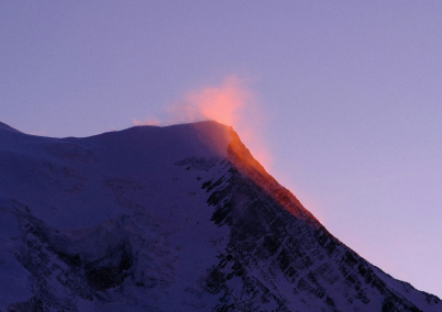 Mountain with purple sky and orange sunlight on a could right above it