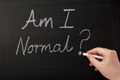 Blackboard with a hand writing “Am I Normal?” in white chalk.