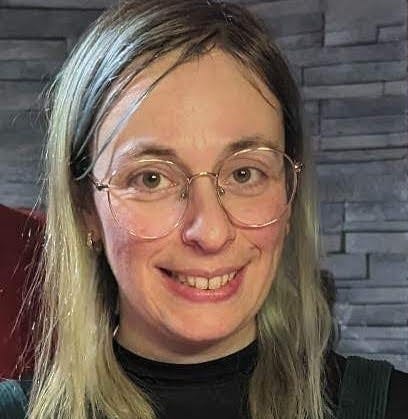 Veronique wearing a black mock-turtle neck and gold wire rim glasses smiling at the camera.