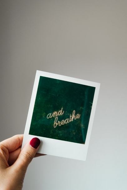 Polaroid being held by a woman that reads “and breathe”