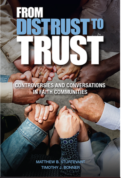 Photo of the book cover of “From Distrust to Trust: Controversies and Conversations in Faith Communities.” The background is a photo from above of only the hands of six different people of various genders and skin tones clasping a hand of the person on each side of them, all facing each other close together, which makes a circle.