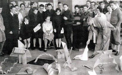 A photo of Josef Albers and his students gathered around innovative paper folding projects at the Bauhaus.