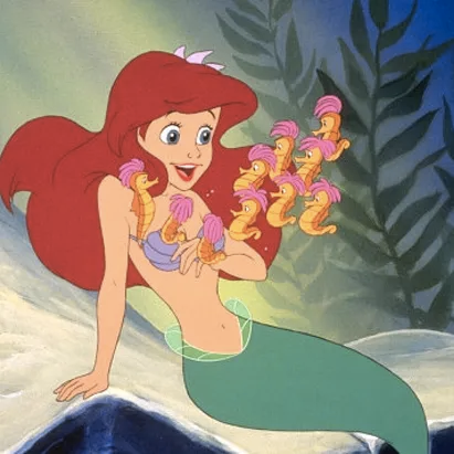 Image of Ariel from the original The Little Mermaid movie. The pale white mermaid with blue eyes and bright red hair is sitting on a rock, talking to a group of small yellow seahorses.