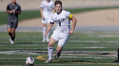 Photo of Captain Lawrence Dydell on the green soccer pitch, mid run. He is wearing an all white soccer outfit, with a soccer ball to his right.