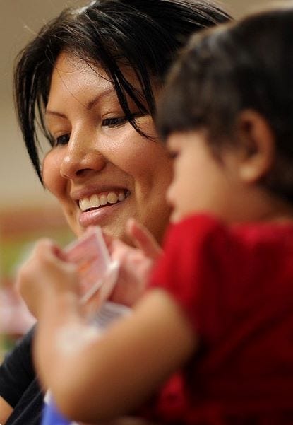 A woman smiling with a child holding cards