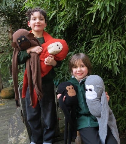 Two boys holding four large monkey puppets in a garden