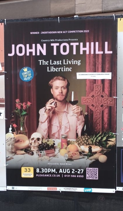 An Edinburgh Fringe poster showing a red-headed white man holding a wine-glass and an apothecary’s bottle. There’s a cross to his left, roses to his right and a mess on the table in front of him, including a pineapple, a human skull, grapes and a female bust.