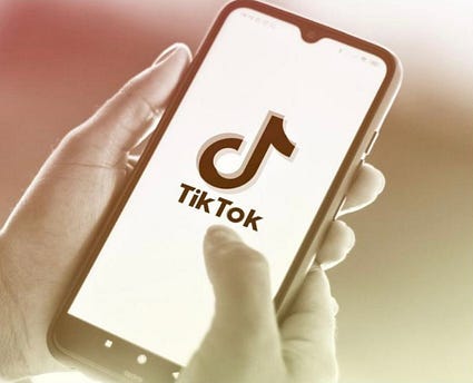 Photo of a hand holding an iPhone. The phone has the TikTok symbol on it.