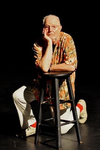 Frank Buxton kneeling behind a stool with his face resting on his right hand