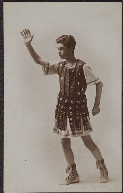 Sepia photograph of a boy dressed in the costume of a Roman soldier with his arm raised in a salute.