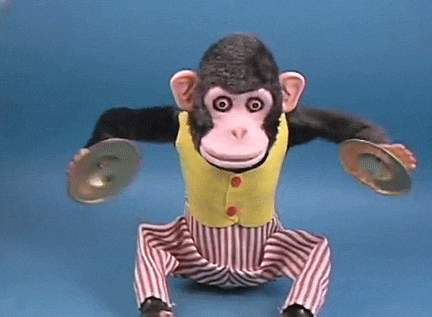 A toy monkey dressed in a vest holds a pair of drums, ready to perform with enthusiasm and charm.
