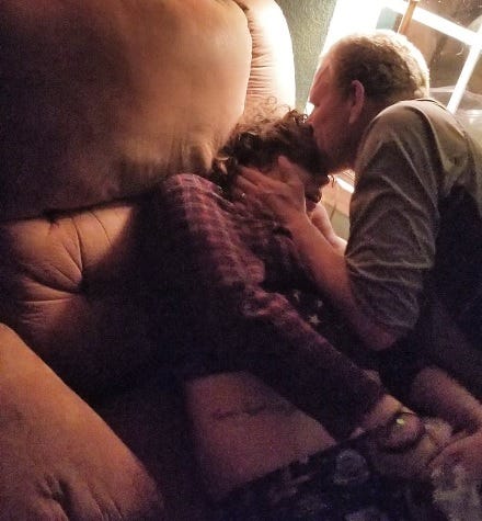 Photo of the author tensed up in an arm chair with a man kissing their forehead.