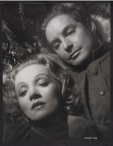 black and white close up film still of the faces of a man and a woman. The woman has curled fair hair and the man is wearing a khaiki shirt with buttons. Both are looking downwards.