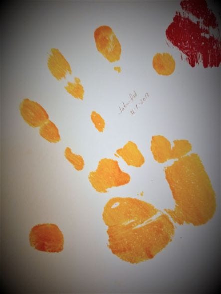 A man’s handprint in yellow paint on a white wall. In pencil is written John/Dad, 31–1–2013.