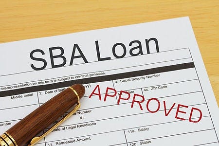 Picture of an SBA Loan application and a ballpoint pen. The application is stamped “Approved” in Red.