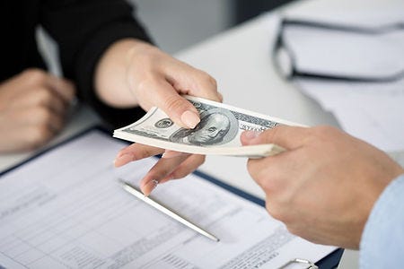 Picture of two hands over a desk exchanging a stack of one hundred dollar bills