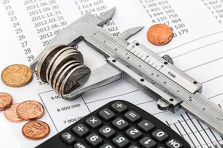 Picture of a measuring tool holding coins on a desk with papewwork and a calculator, signifying you should consider all the finacning options carefully to choose the right option for your dental practice.