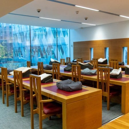 The Reading Room at the John Rylands Library with wooden desks and chairs. There is a book pillow and foam supports on each of the desks.