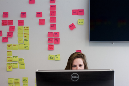 Person sitting behind a computer monitor in front of a wall of post-its