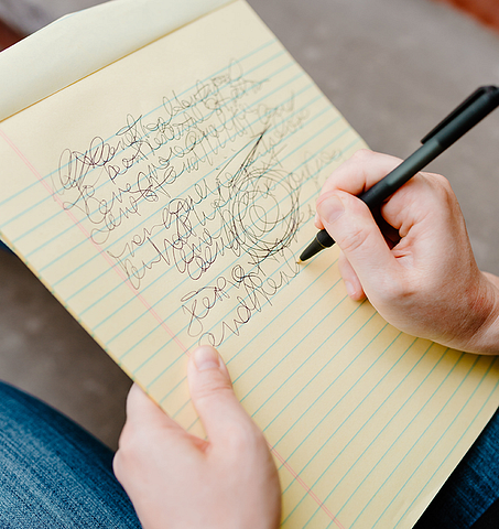 photo of a hand scribbling illegible words on a legal pad.