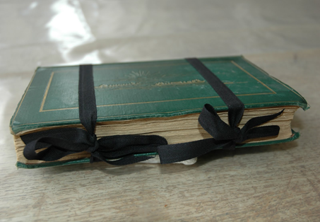 A green book tied together by two black bows.