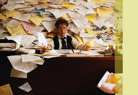 A guy swamped with tasks and sticky notes looking overwhelmed