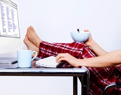 Man with feet up on a desk, legs in pajama pants, holding a bowl of cereal