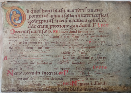 Front board of a book covered in a light brown parchment binding. The binding has neat twelfth century handwriting in red and black with a gold letter O in a blue background with a floral motif