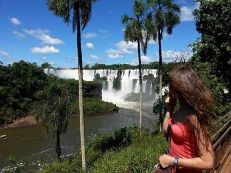 A girl in a pink tank top looking over the Iguazu River and layers of waterfalls beyond
