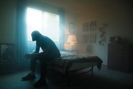 Depressed man sitting on his bed in a dimly lit room