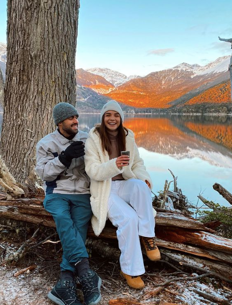 They are posing in front of a lake in ushuaia, in winter clothes, laughing and enacant. The colors of the video are autumnal.