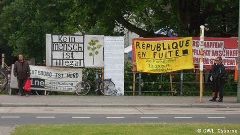 Colorful banners and posters reading different asylum seeking protest sayings in German.