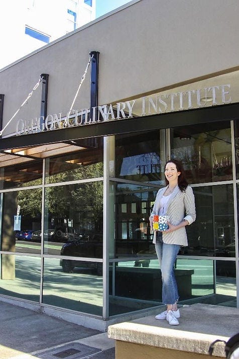 Katie Poppe standing in front of the Oregon Culinary Institute holding a box of packaged Blue Star donuts.