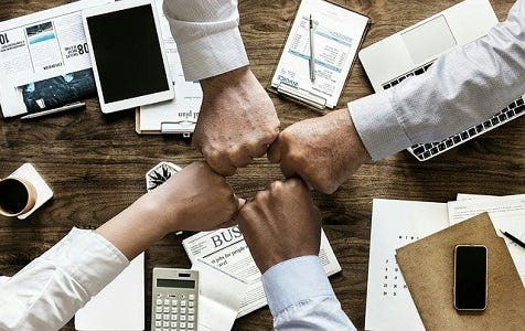 Image of four fists over a meeting table making a four-way fistbump.