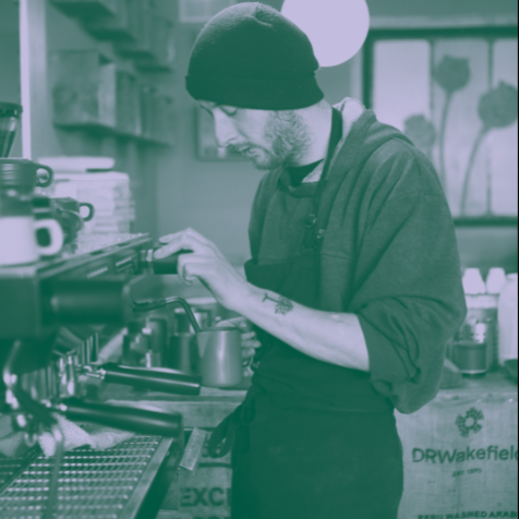 Caption: A man wearing a beanie makes a coffee at a coffee machine