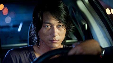 Sung Kang as Han in The Fast & The Furious: Tokyo Drift. He is driving a car and looking determined.