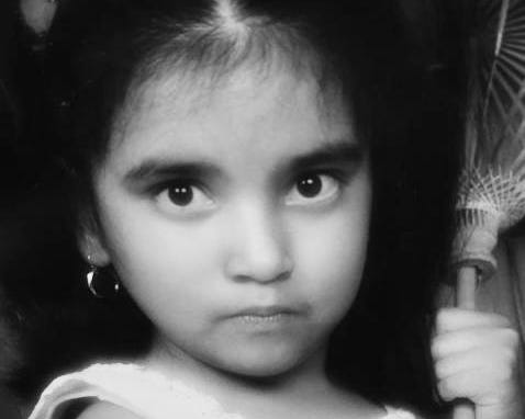 Black and white photo of a little girl wearing a sleeveless dress holding an umbrella