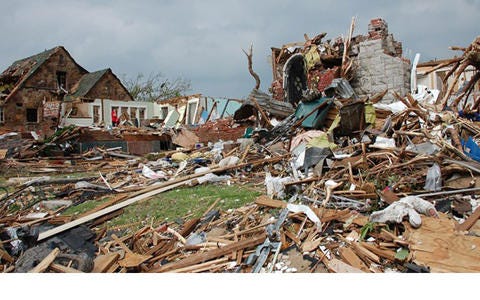Tornado damage includes a building mostly destroyed with wood and other debris spread around it.