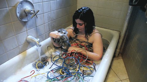 Woman in a bathtub covered in ethernet cables and trying to casually untangle them