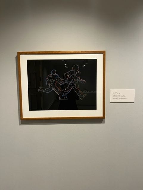 A picture on a gallery wall. The pictures includes two figures holding hands while running.