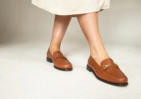 Shot of legs in brown loafers and off-white skirt