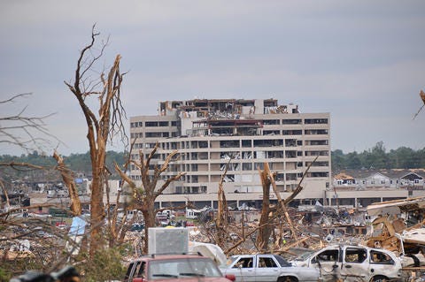 Damaged hospital building in the distance with piles of debris and wrecked cars in the foreground.