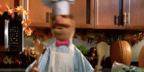 The Swedish Chef character from the muppet dances in the kitchen with two wooden spoons.