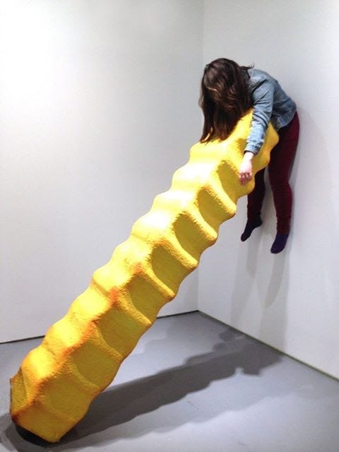 A giant french fry leans against a wall. Between the two, a person is trapped (a nod to another art piece).