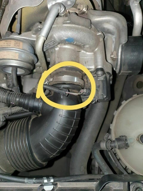 Un tubo de admisión de plástico negro con una fisura en la entrada del turbo, que es una pieza de fundición gris (metal muy ligero). La rotura ha sido señalada con un círculo amarillo.